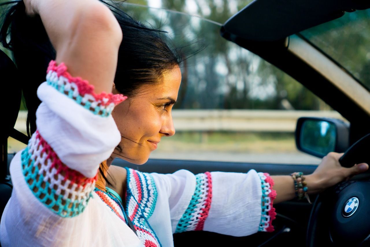 A woman is sitting in a car with her hands in her hair.