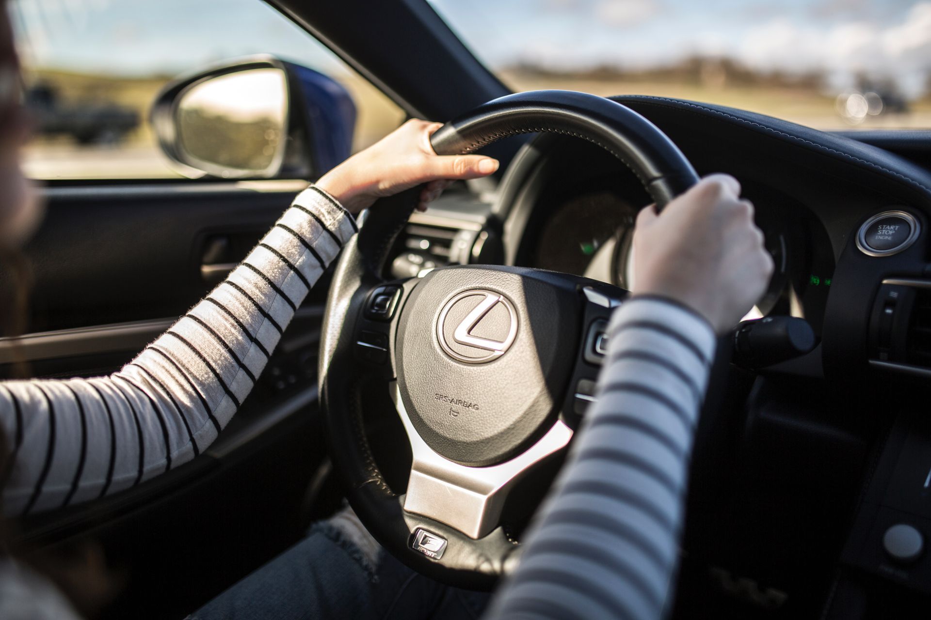 A woman is driving a lexus car with her hands on the steering wheel.
