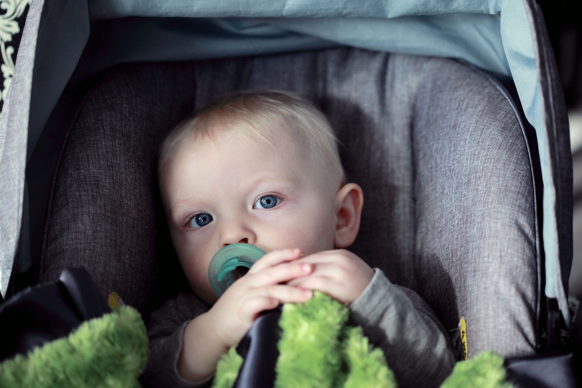 A baby is sitting in a car seat with a pacifier in his mouth.