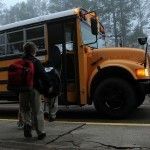 A school bus is parked on the side of the road in the rain.