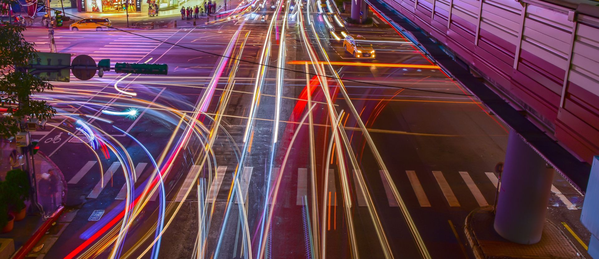 A long exposure of a city street at night with a bridge in the background.