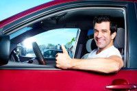 A man is sitting in a red car giving a thumbs up.