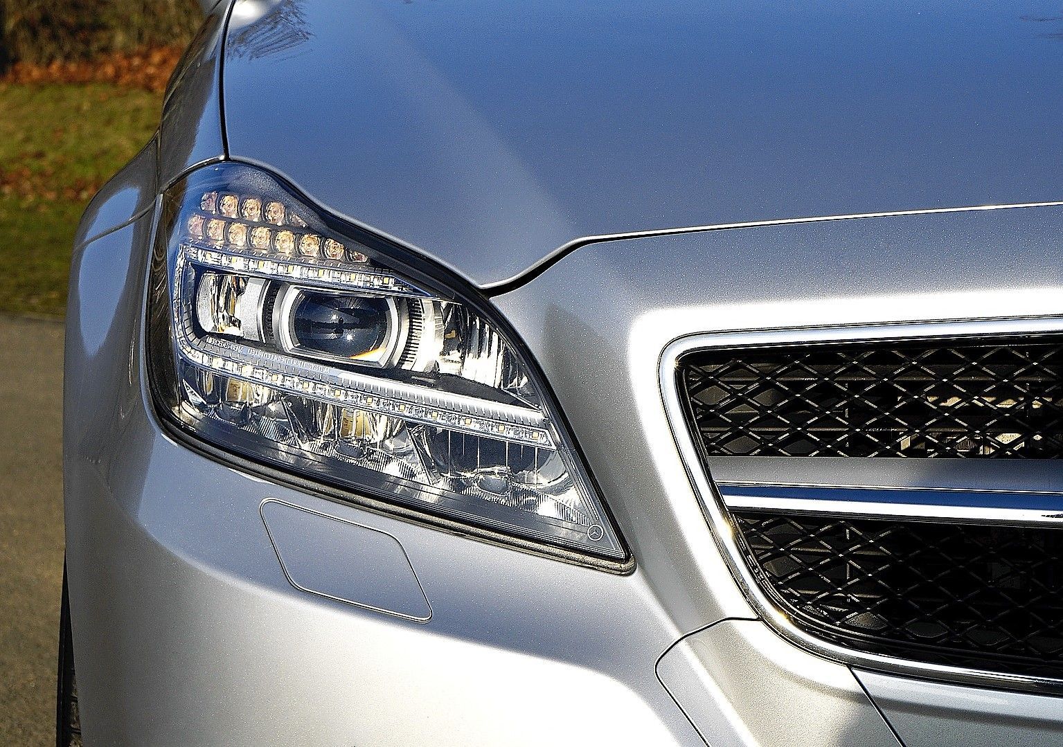 A close up of a silver car 's headlight and grille
