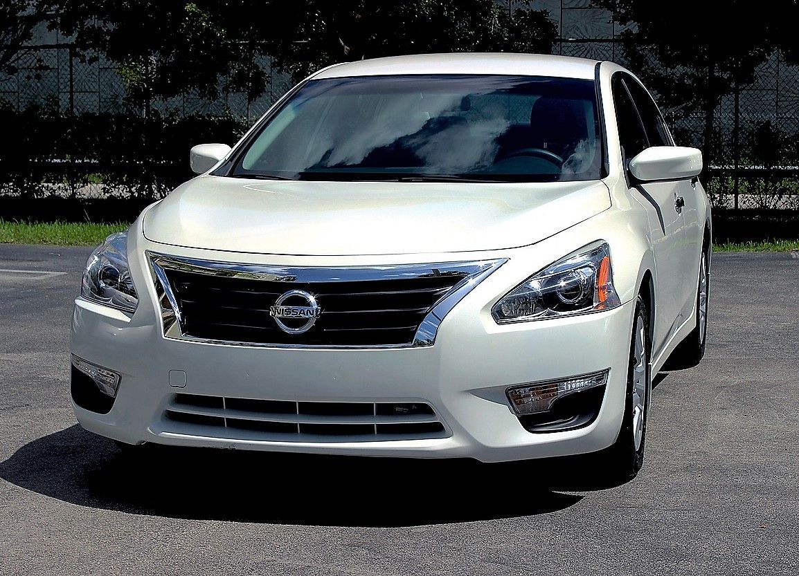 A white nissan altima is parked in a parking lot