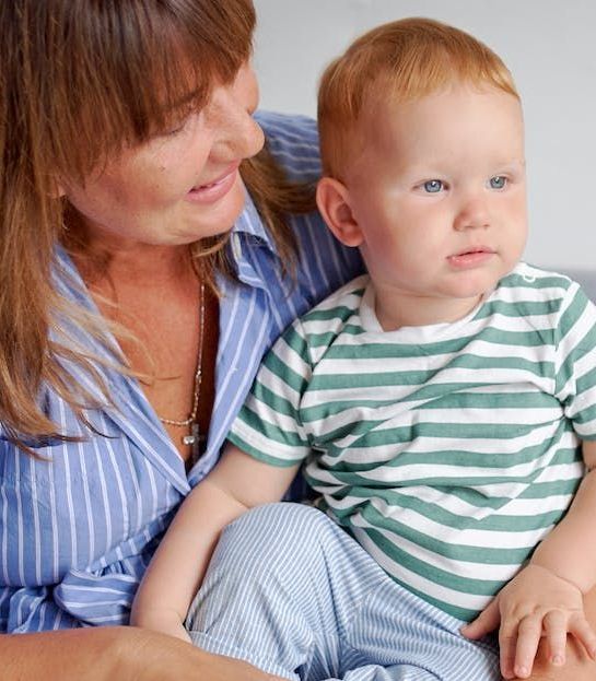 A woman is holding a baby wearing a green and white striped shirt