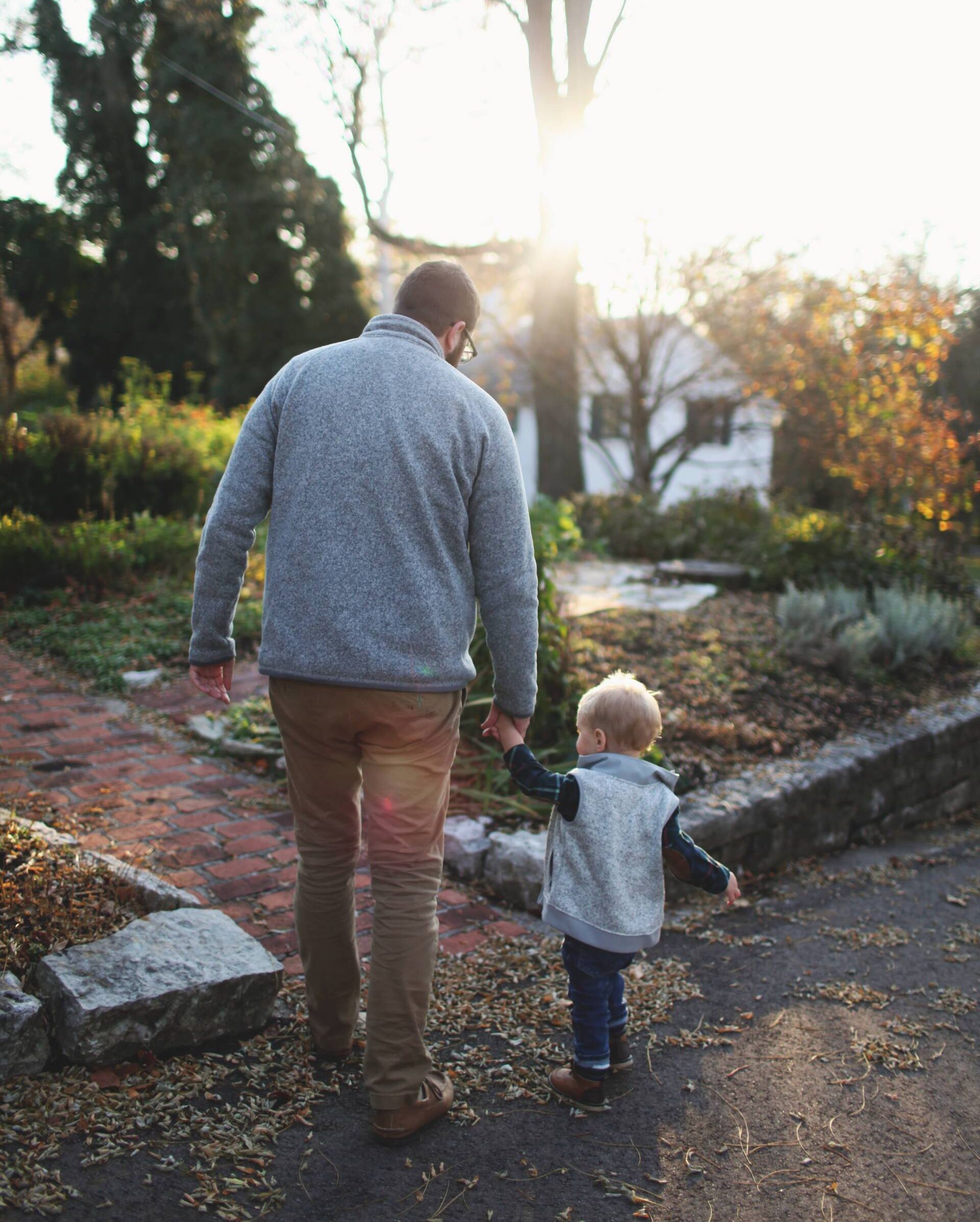 A man and a child are walking down a path holding hands.
