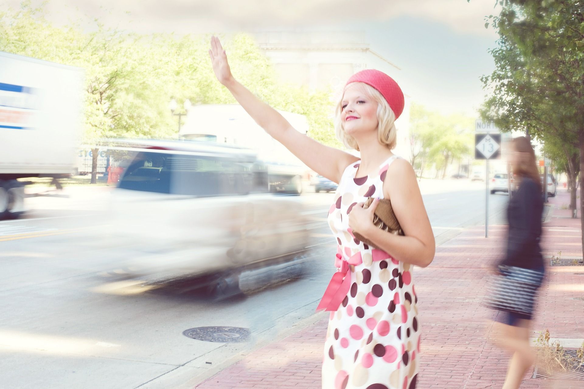 A woman in a polka dot dress is hailing a taxi.