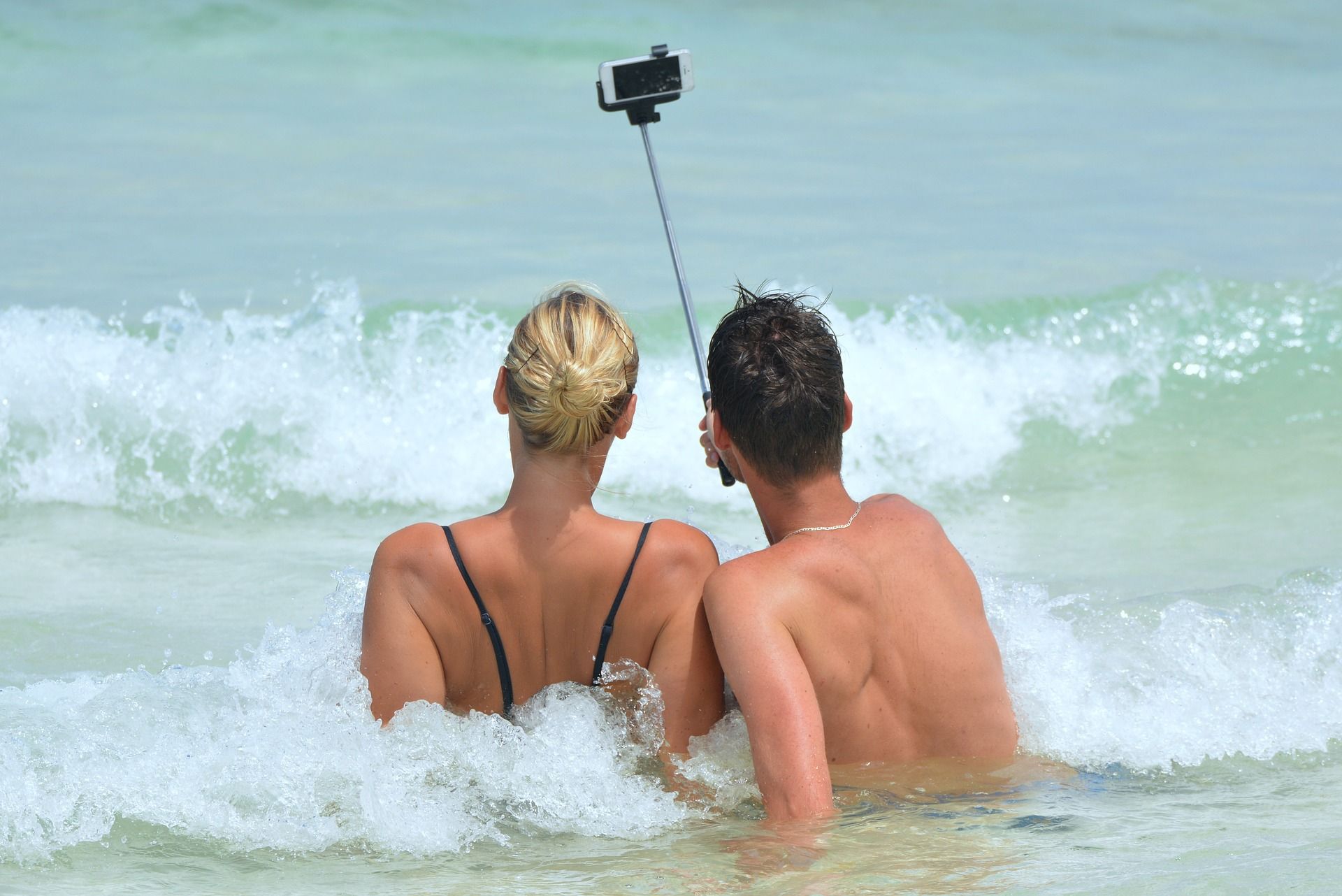 A man and a woman are taking a selfie in the ocean.
