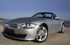 A silver bmw z4 convertible is parked on the beach next to the ocean.