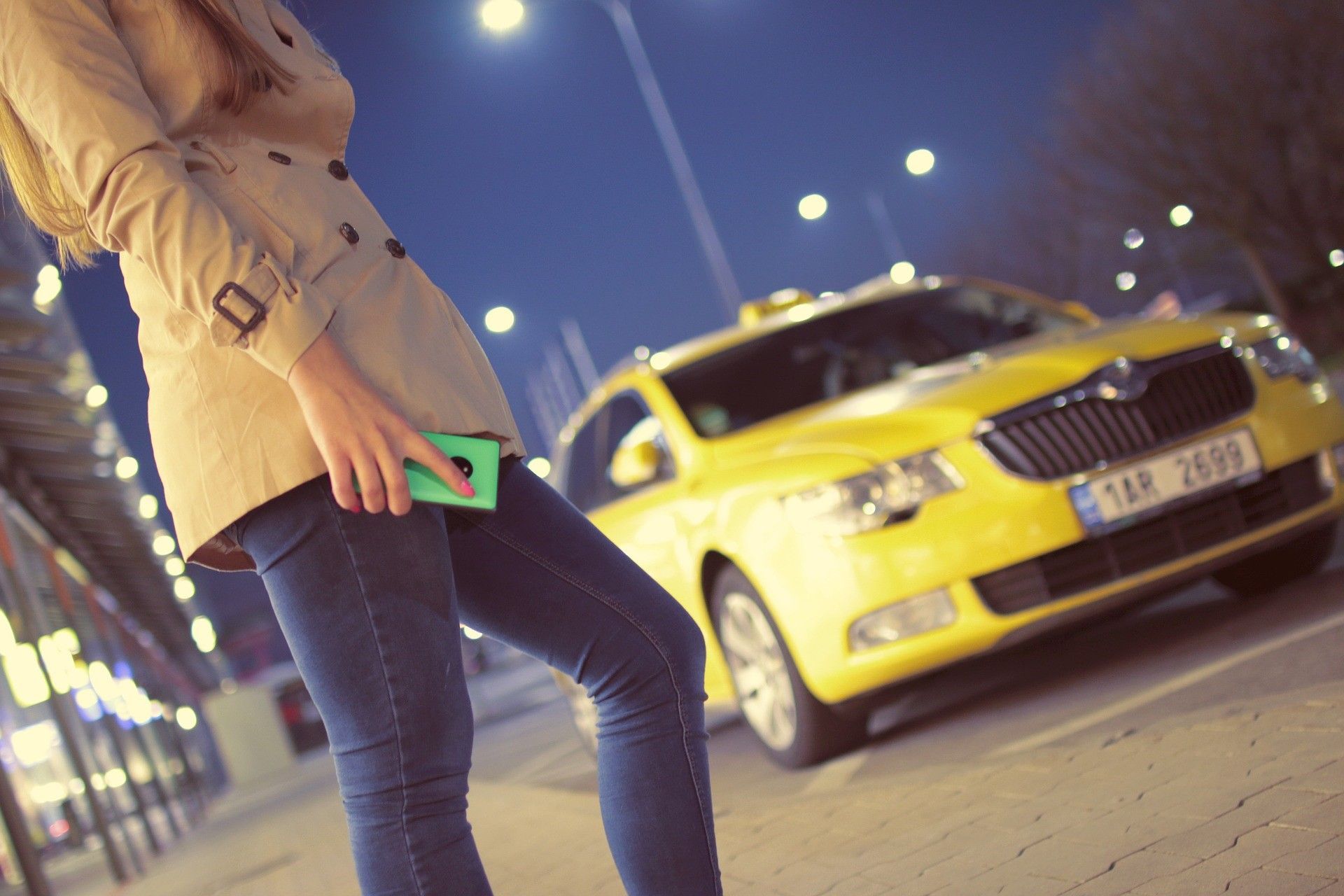 A woman is standing in front of a yellow taxi.