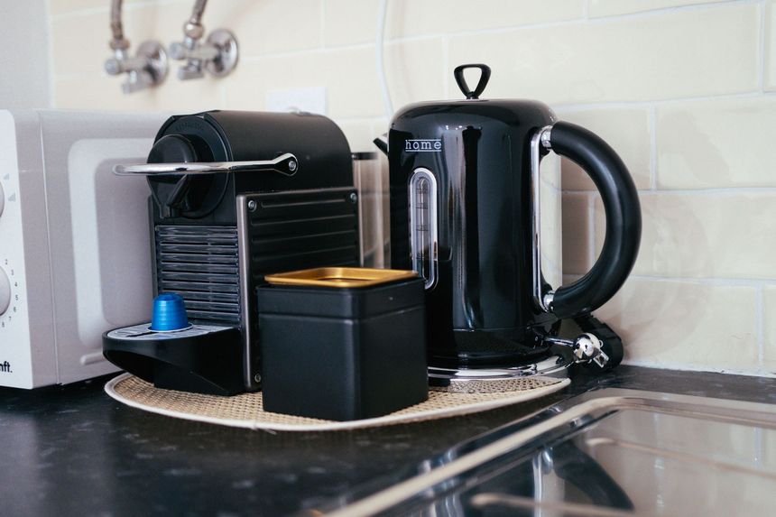Black coffee machine, electric kettle, and cup on a kitchen countertop with tiled backsplash