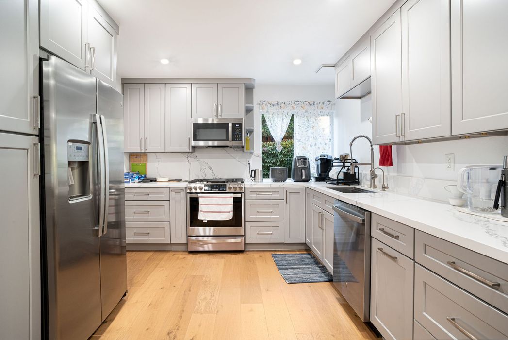 Bright modern kitchen with white cabinets, stainless steel appliances, and light wood floors