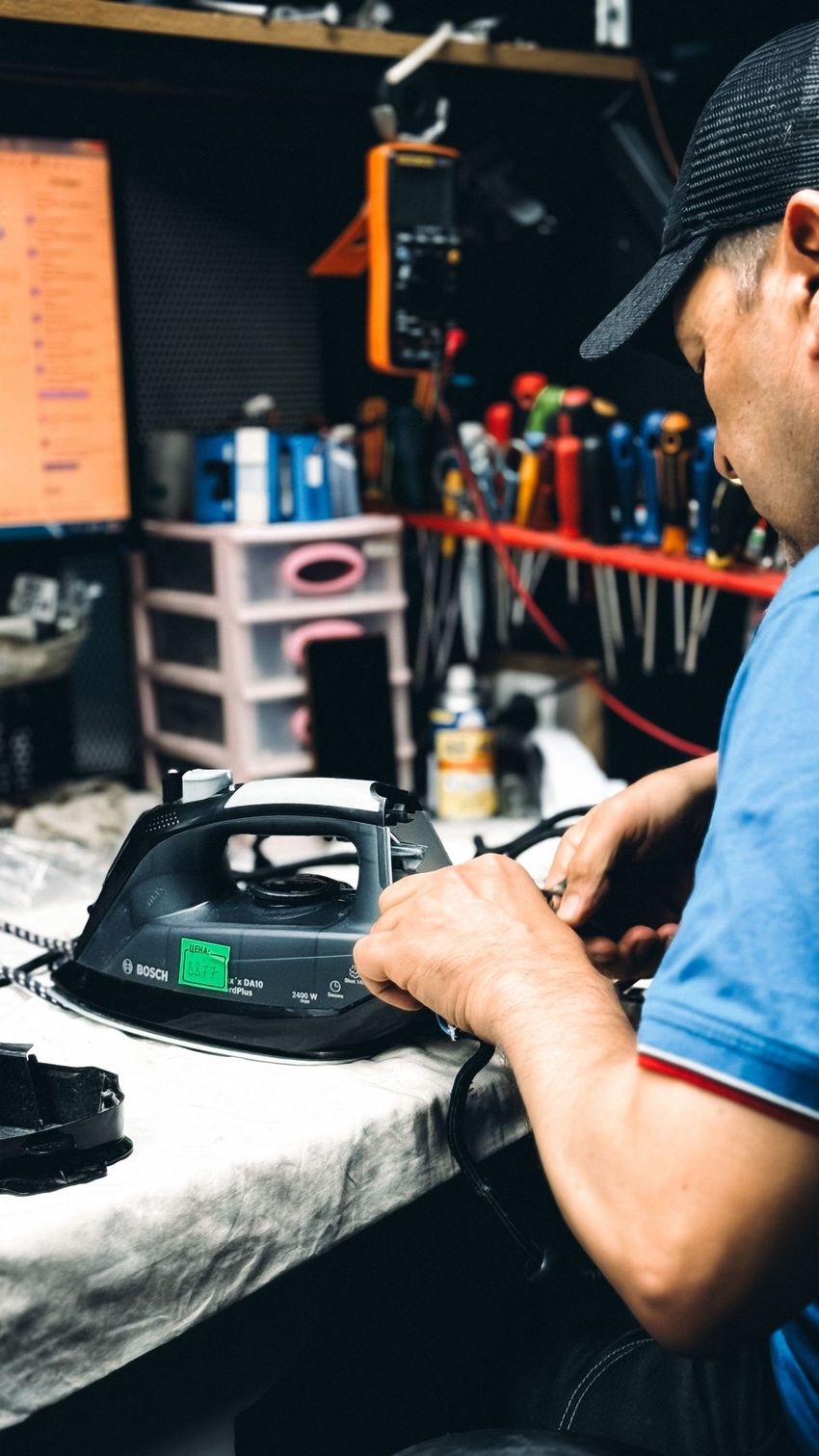 Person in a workshop repairing a speaker on a workbench, with tools and shelves in the background.