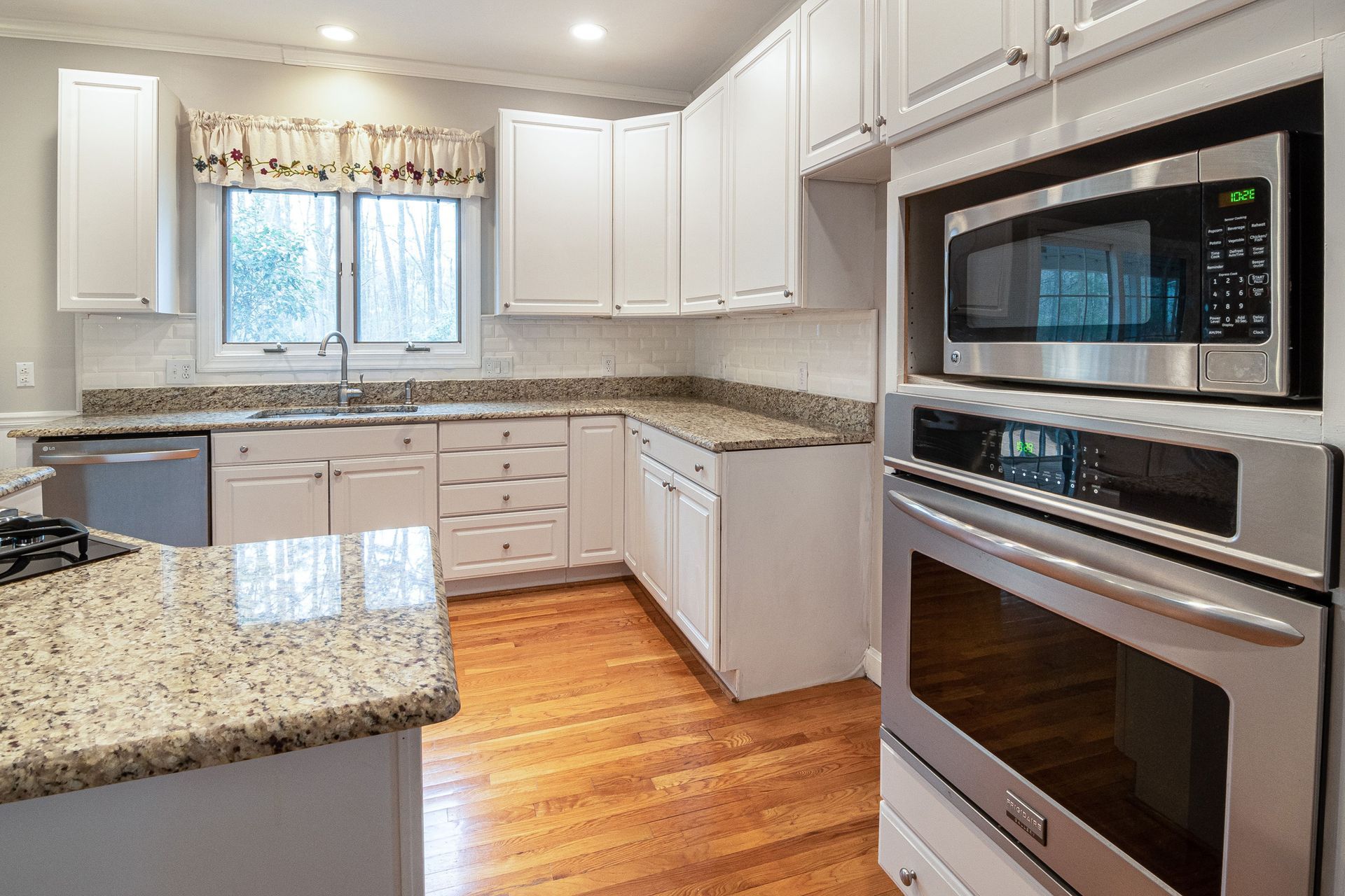 Bright kitchen with white cabinets, granite countertops, wood floor, and stainless steel oven and microwave.