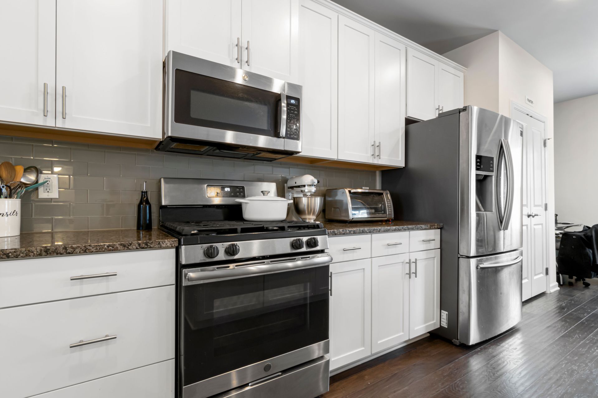 Modern white kitchen with stainless steel appliances, dark countertops, and dark wood flooring