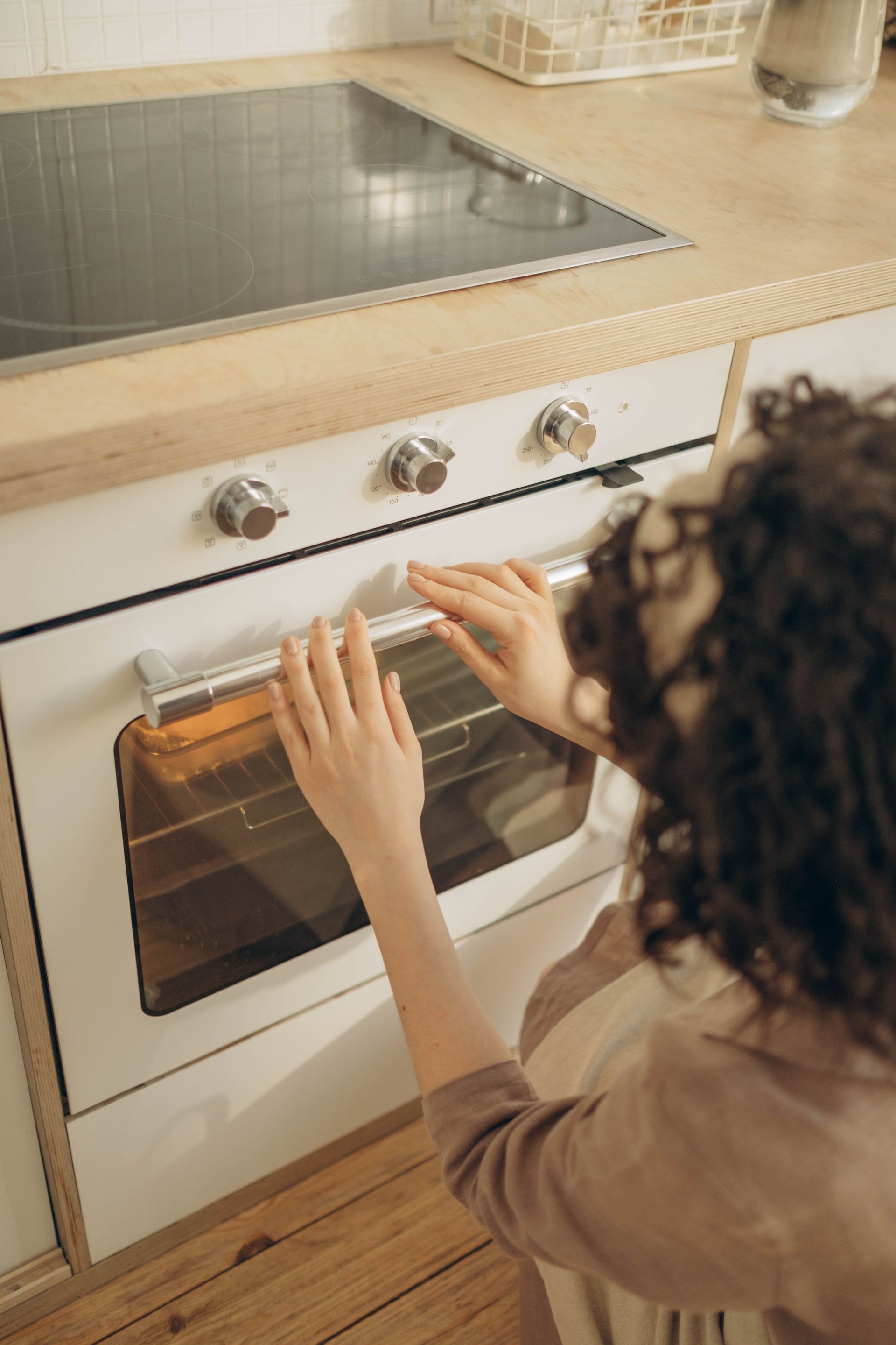 Person placing a tray into a white oven in a modern kitchen