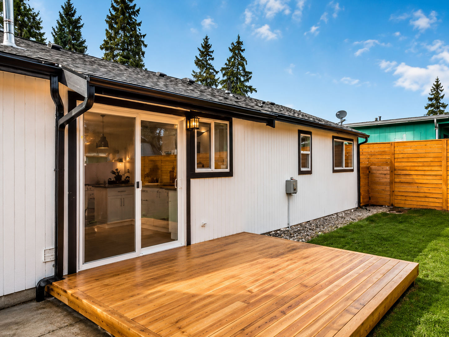 Wooden deck outside a white house with sliding glass doors and a fenced backyard