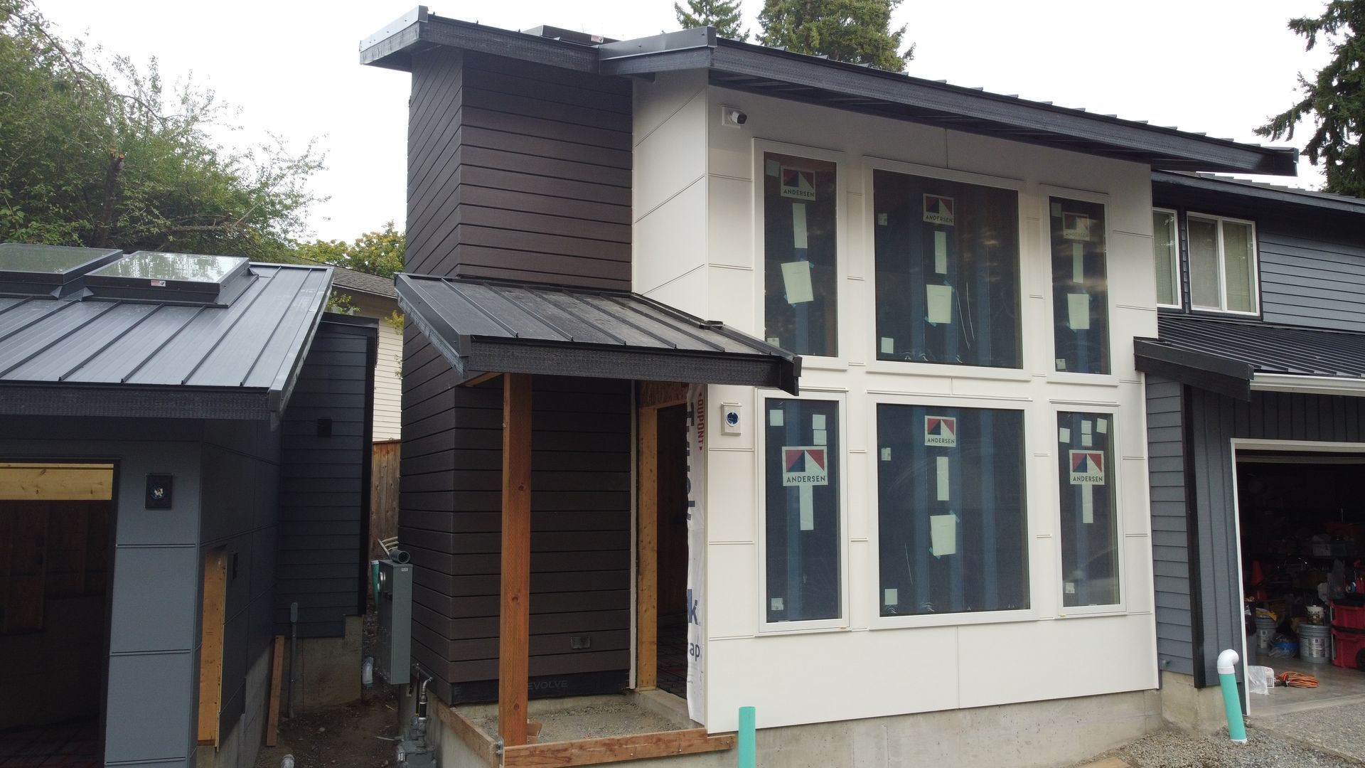 Two-story house exterior with white siding, dark brown upper walls, and large windows under construction