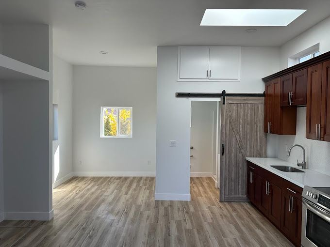 Empty modern kitchen and dining area with wood cabinets, light flooring, and a small window.