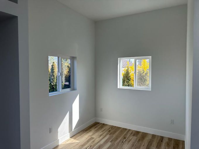 Empty white room with two windows and sunlight on the floor, wood flooring and gray walls