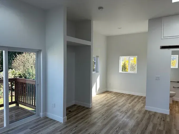 Empty modern living room with sliding glass door, light gray walls, and wood-look flooring