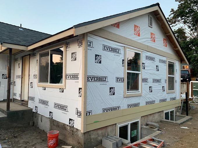 Partially built house with white house wrap, windows, and a front gable under construction