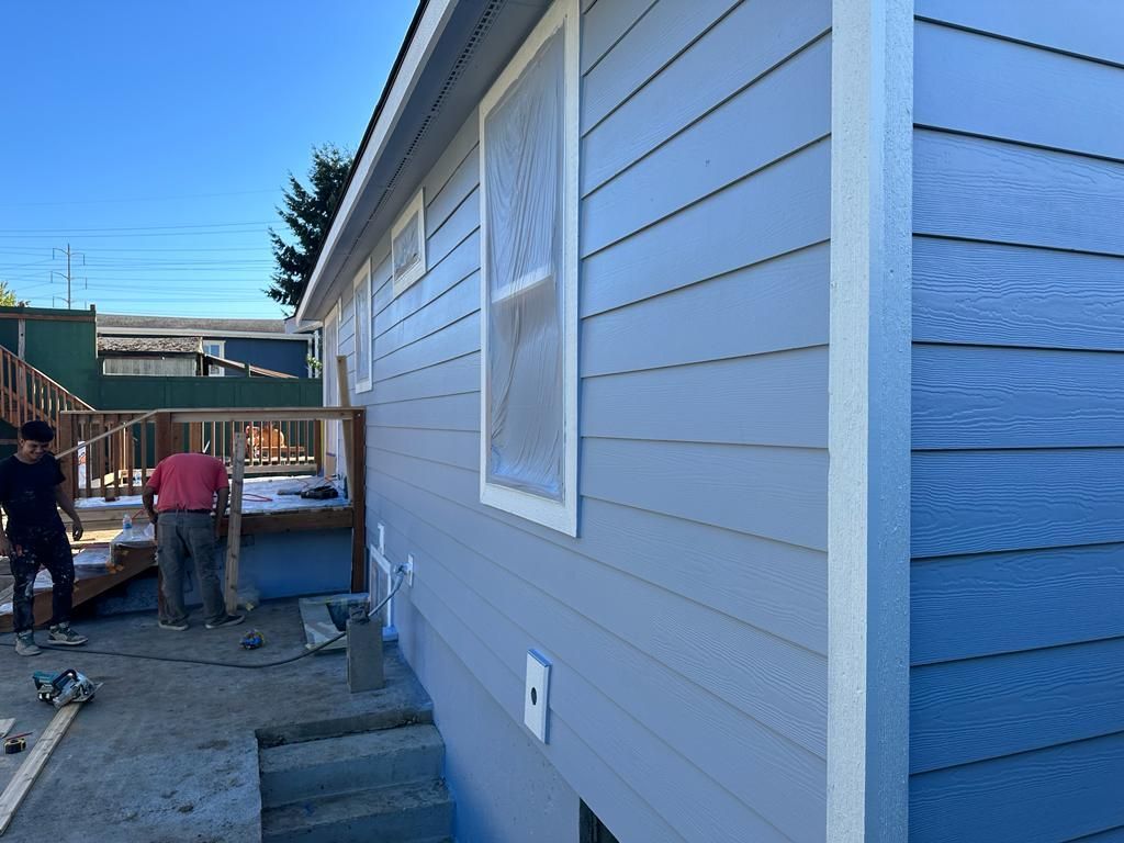 Side view of a light gray house under construction, with workers and tools along the driveway.