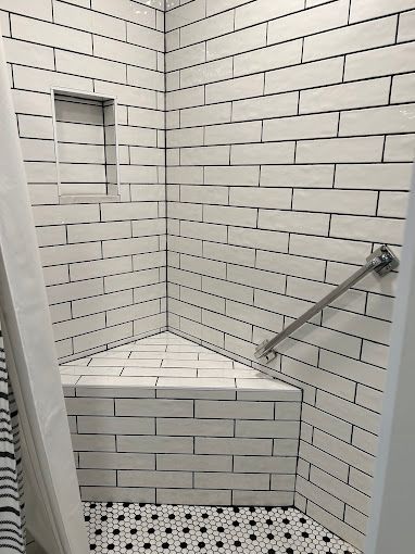 Empty tiled shower stall with built-in bench, wall niche, and stainless steel grab bar.