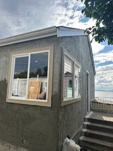Small gray building by stairs with a window, under a partly cloudy sky near the water.