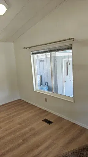 Empty room with white walls, wood floor, and a large window showing an exterior utility area