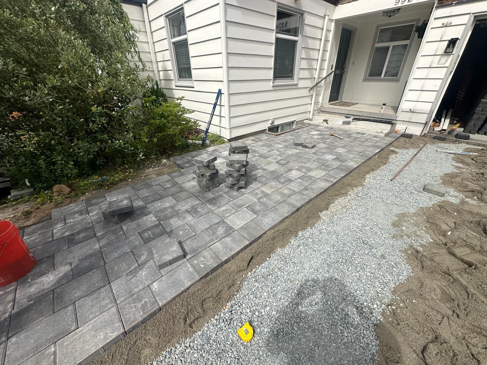 Paved walkway and gravel path beside a house entrance, with a small yellow marker on the ground.