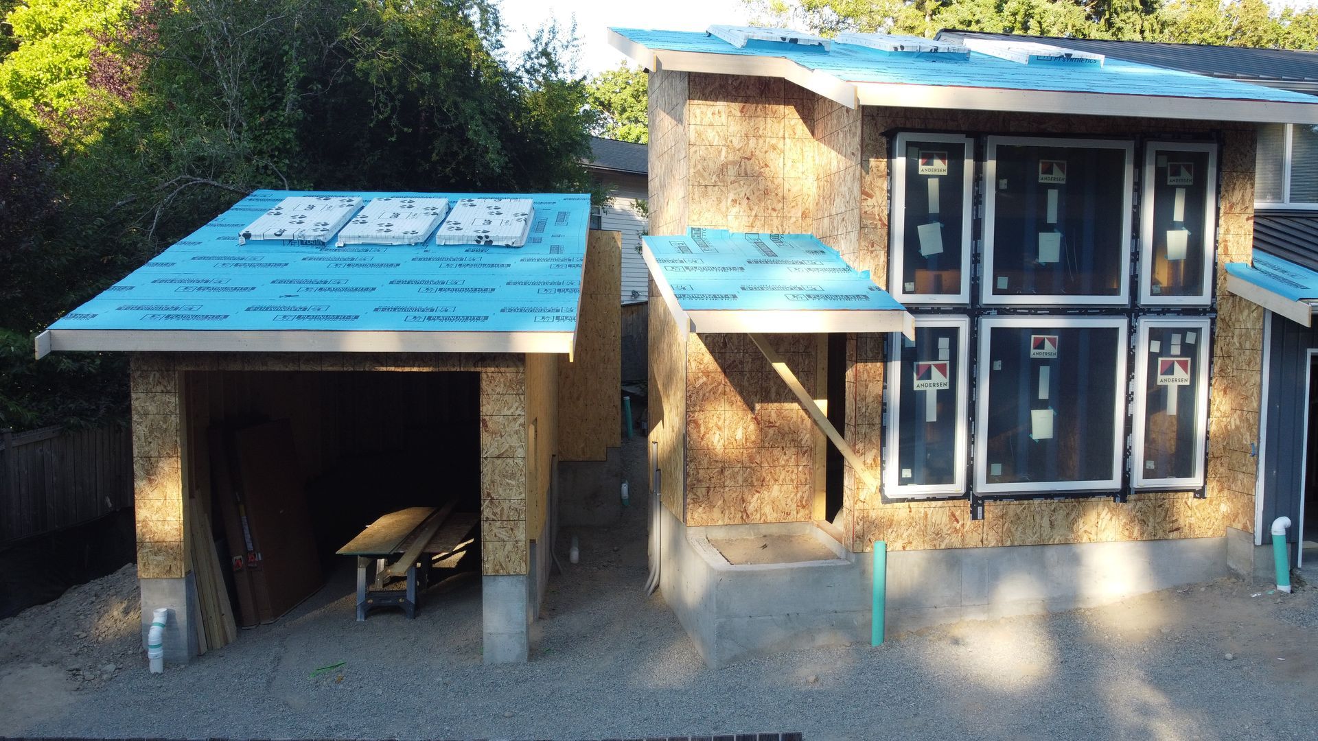 Two small blue-roofed shelter structures in a gravel yard, one open and one with black doors and windows.