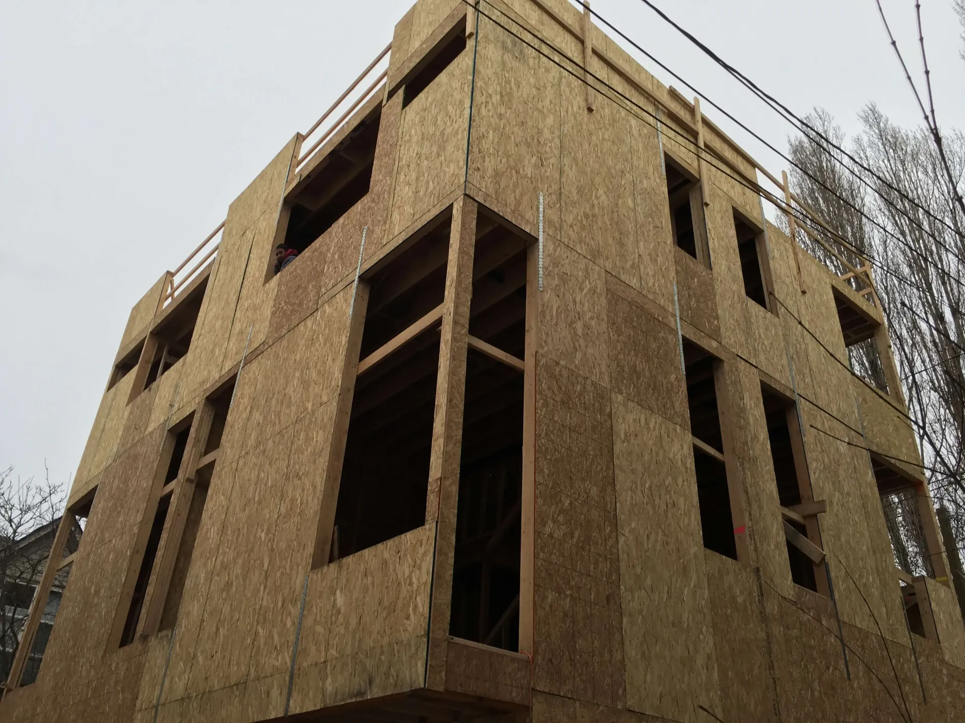 Unfinished plywood building under construction, viewed from below against a cloudy sky
