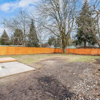 Empty fenced backyard with bare trees, orange privacy fence, and a concrete slab under a clear sky