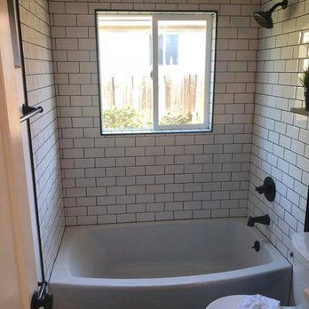 Empty white-tiled bathroom with a bathtub, shower fixtures, and a window above the tub