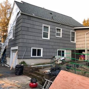 Gray two-story house with new siding and windows under construction, ladders and tools in yard