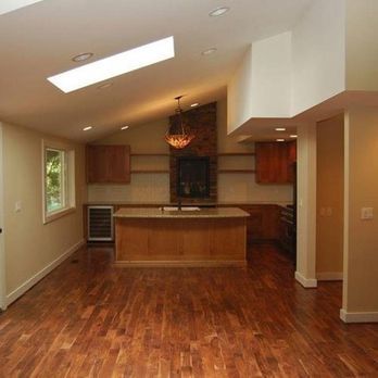 Empty modern kitchen with wood floors, island, skylight, and a brick backsplash