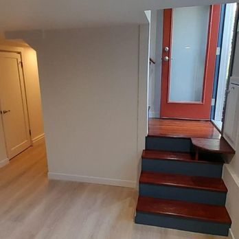 Interior hallway with light wood floors and a short staircase leading to a red door.