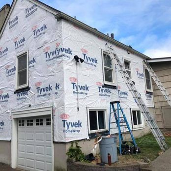 House under renovation wrapped in Tyvek, with ladders leaning against the exterior and a garage below.