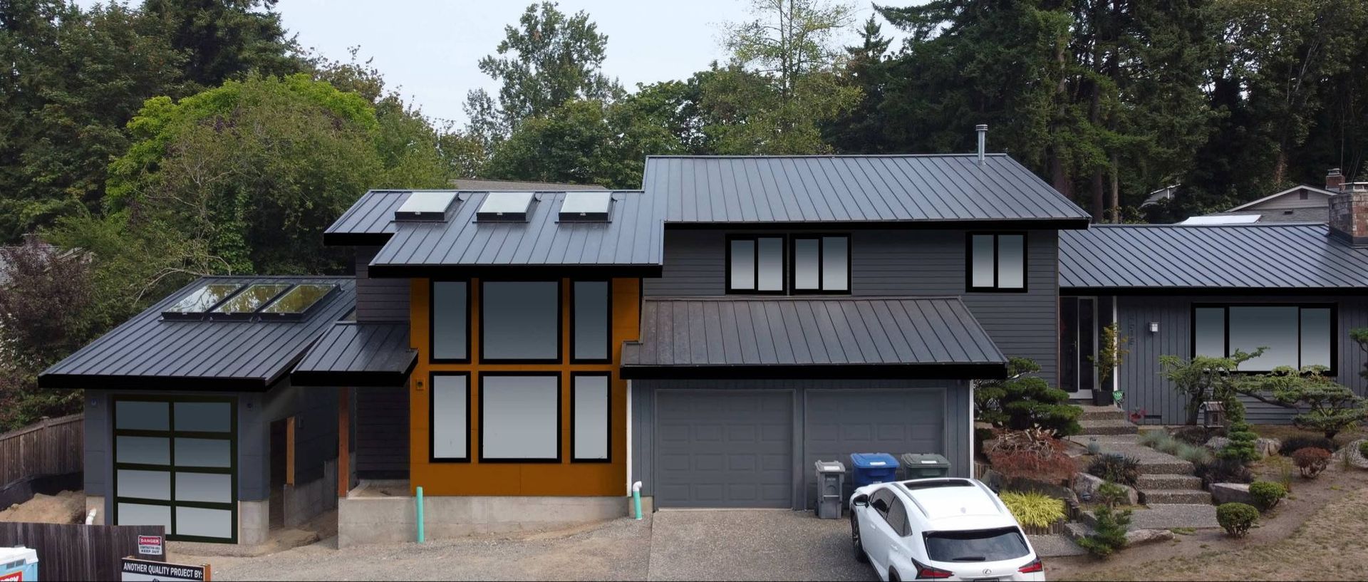 Modern two-story gray house with skylights, wood accents, and a white car in the driveway