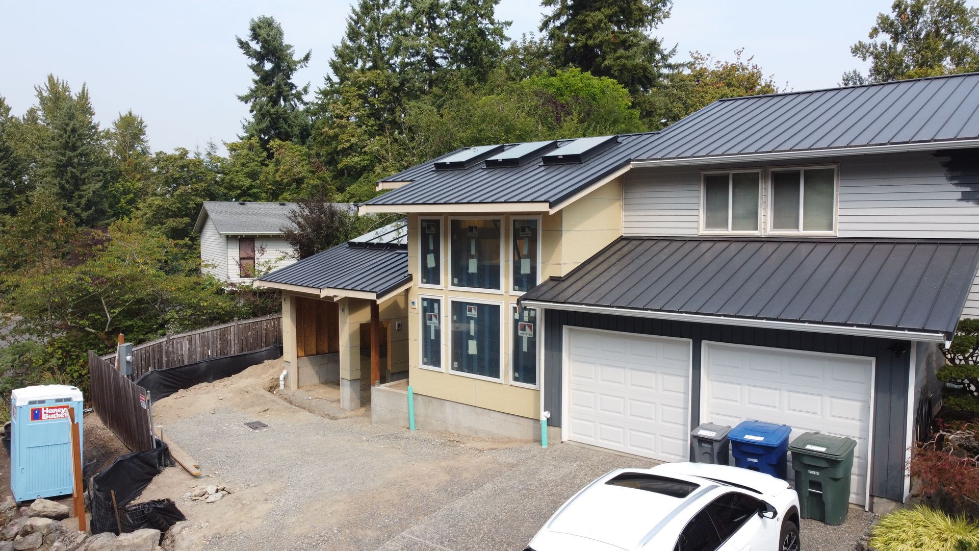 Modern house with black metal roof, solar panels, garage, gravel driveway, and parked vehicles.
