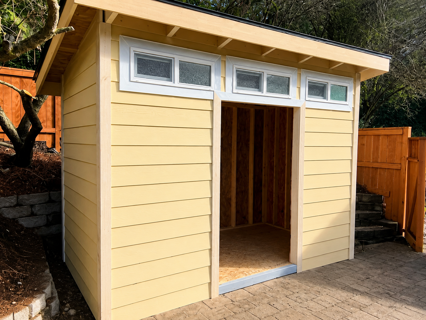 Small yellow garden shed with white trim and open doorway on a paved yard