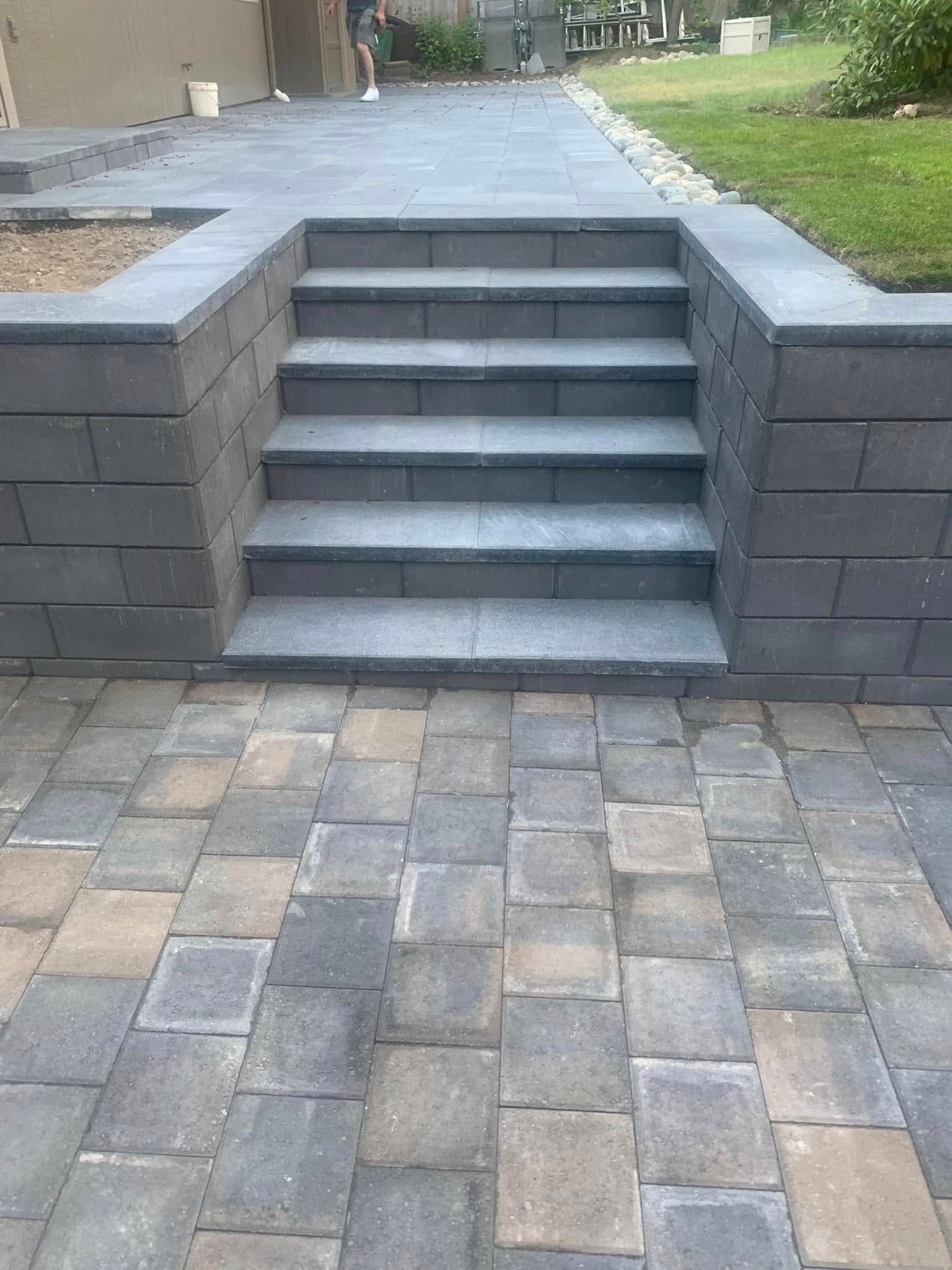 Stone patio steps leading up to a raised walkway beside a lawn.