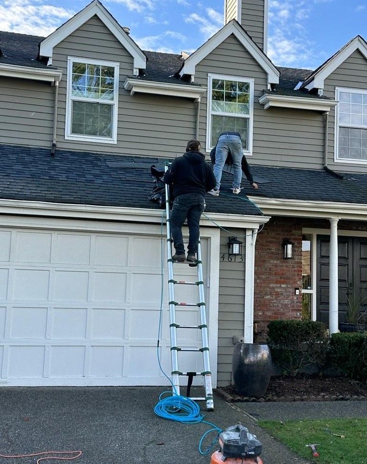 Two workers on a ladder repairing the roof above a garage on a suburban house