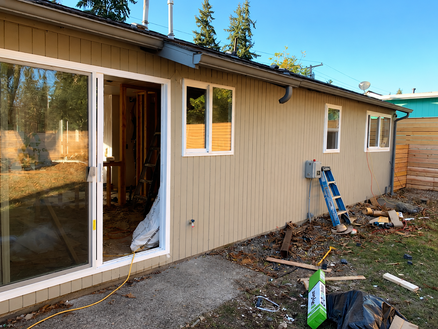Side of beige house with sliding glass door, open entry, and ladder leaning near the wall.