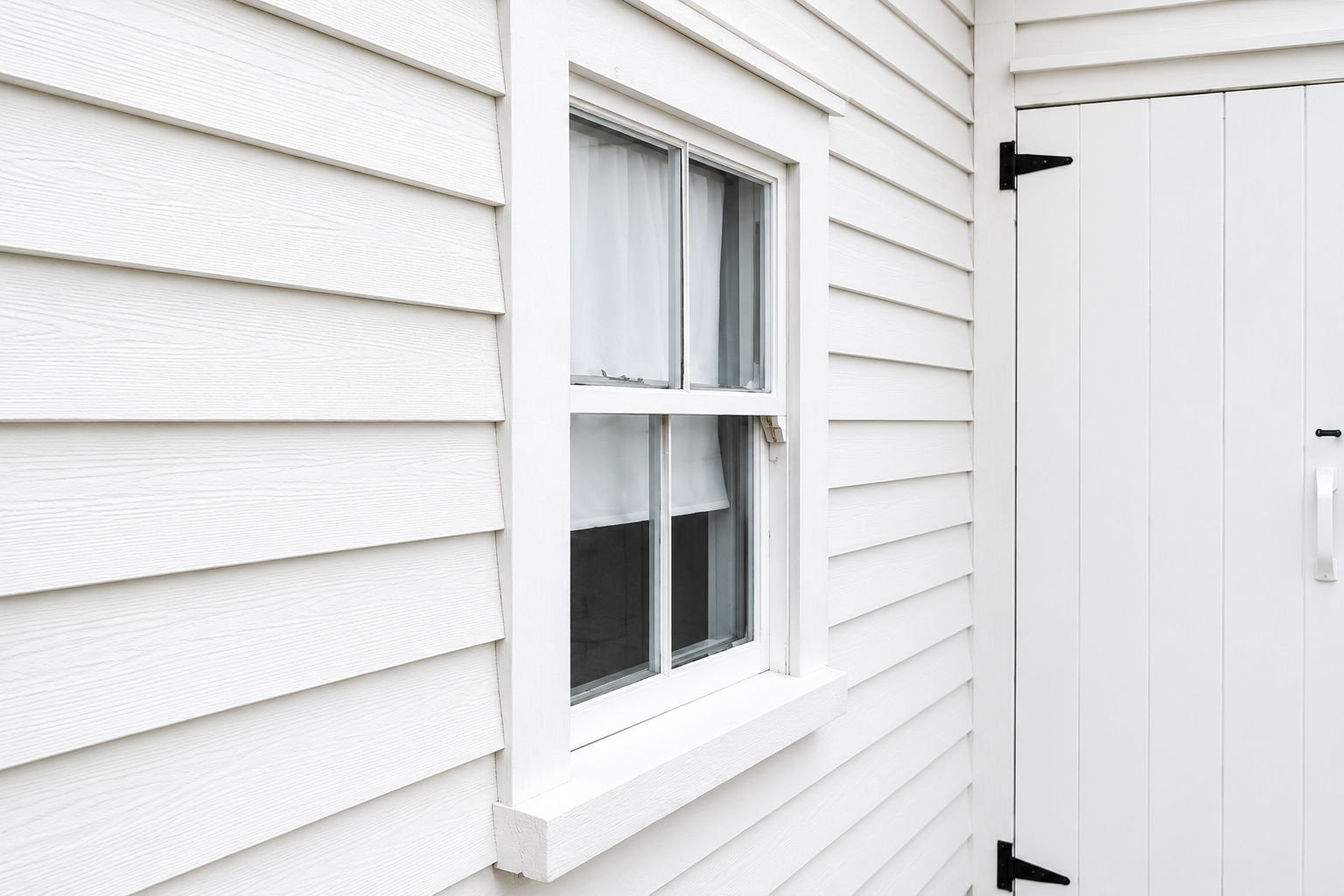White house siding with a small window beside a white door with black hinges