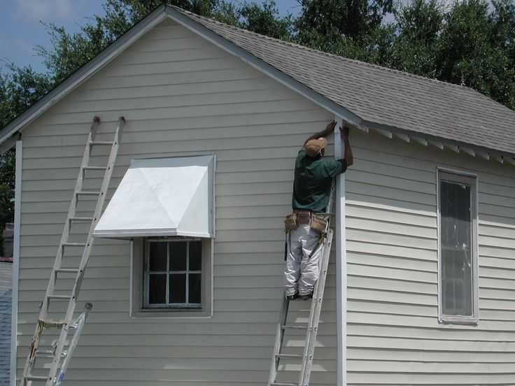 Worker painting the trim of a gray house while standing on a ladder