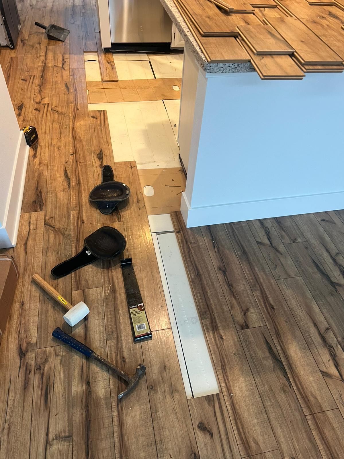 Kitchen floor with scattered tools and debris near a cabinet and doorway, suggesting renovation or cleanup