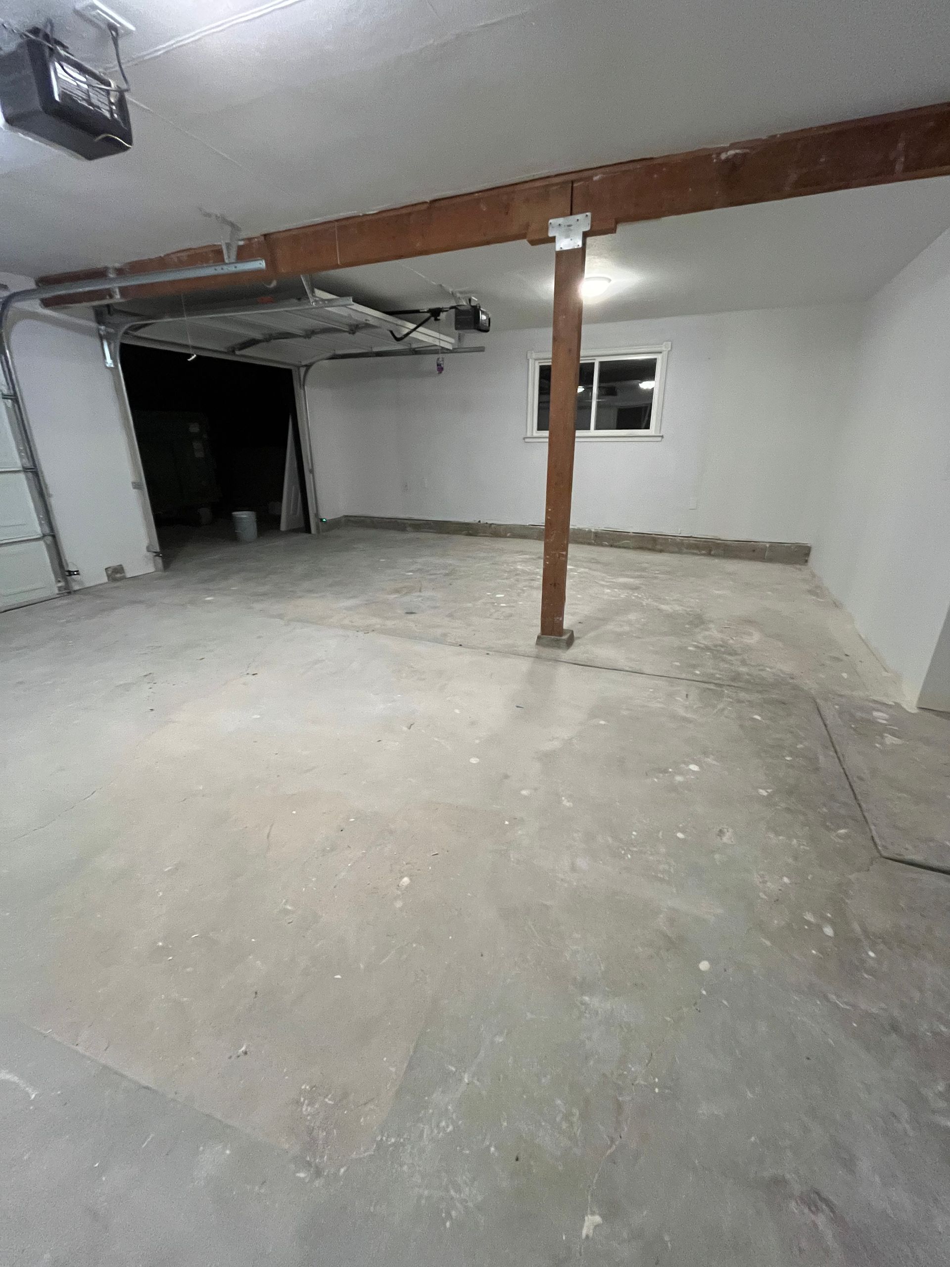 Empty unfinished basement with concrete floor, exposed beam, and a small window on the right.