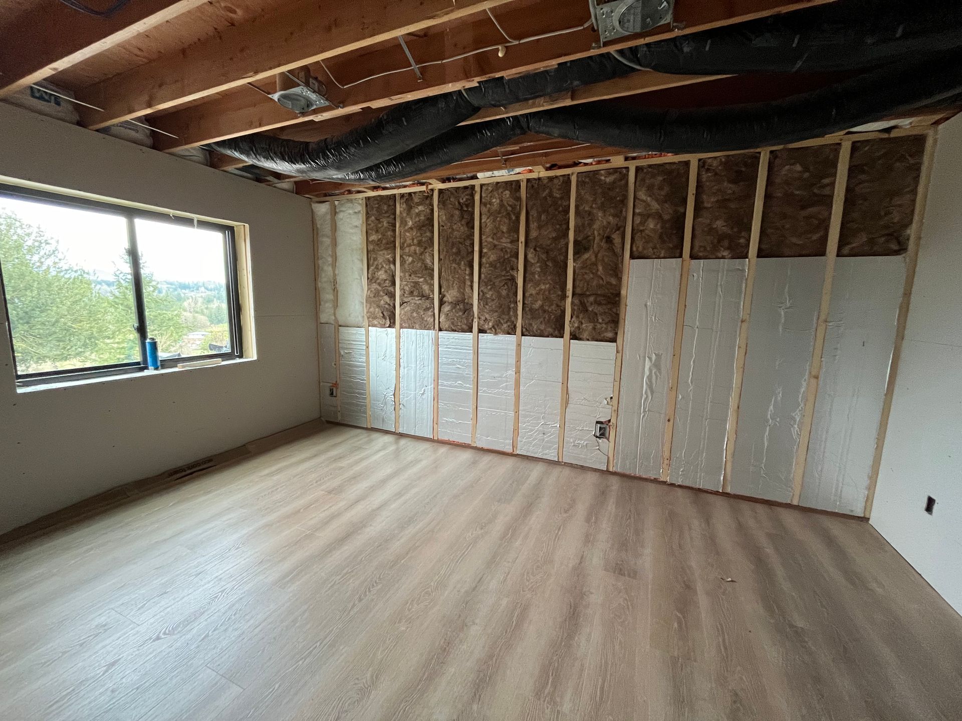 Empty unfinished room with exposed insulation, slanted ceiling, and a large window.